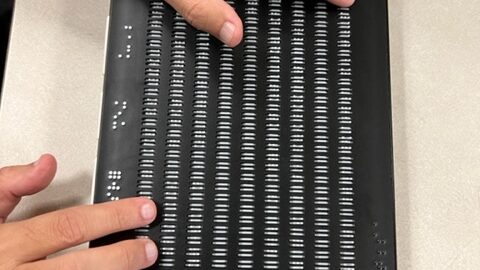 Foto del Canute 360, una multi-línea Braille de página completa que integra 9 líneas de 40 celdas. La foto muestra las manos de Manolo leyendo en la unidad.