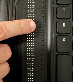 Foto de un dedo leyendo sobre una línea Braille.