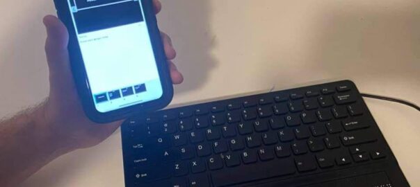 Foto de un iPhone con el app de power Point y al lado un teclado tipo QWERTY que integra una línea Braille