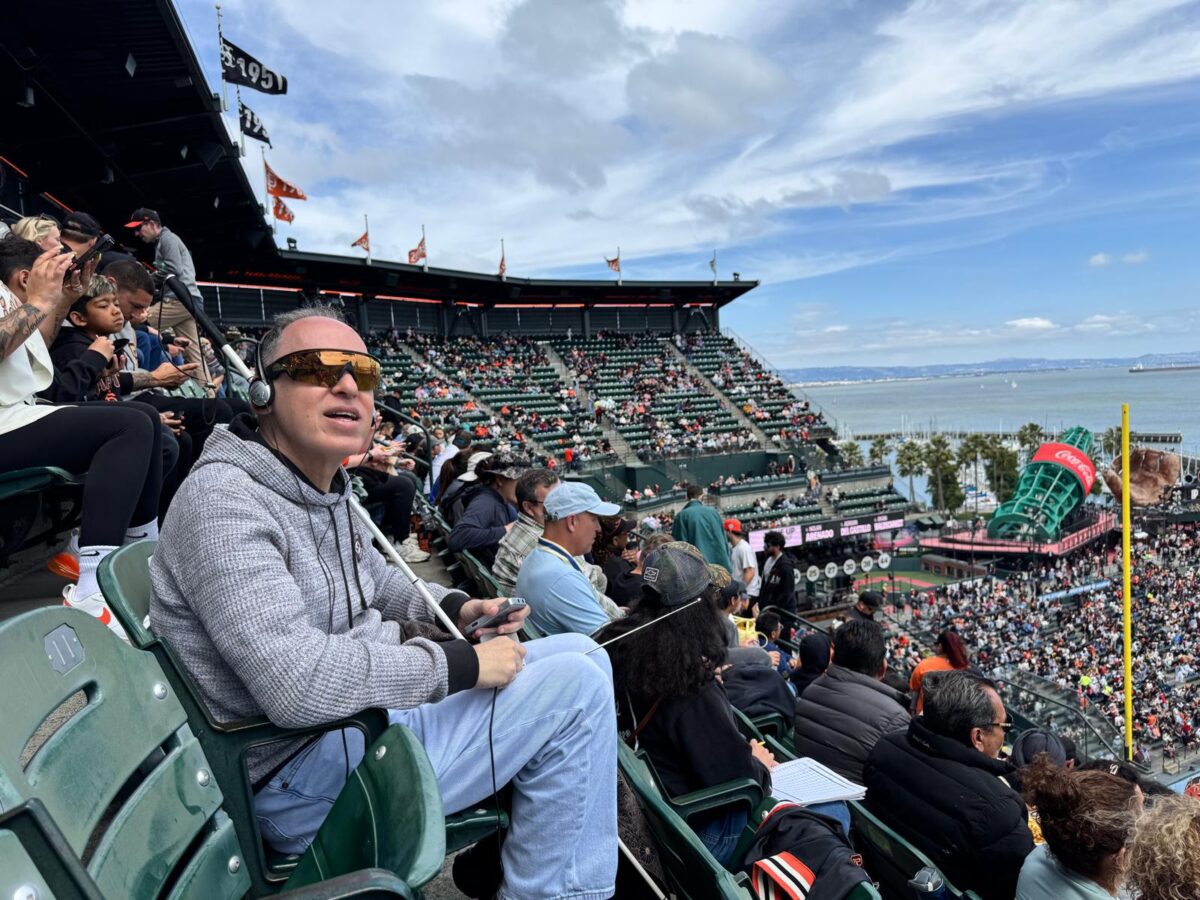 Manolo en las gradas del estadio de baseball de los Gigantes de San Francisco escuchando el juego con audífonos.