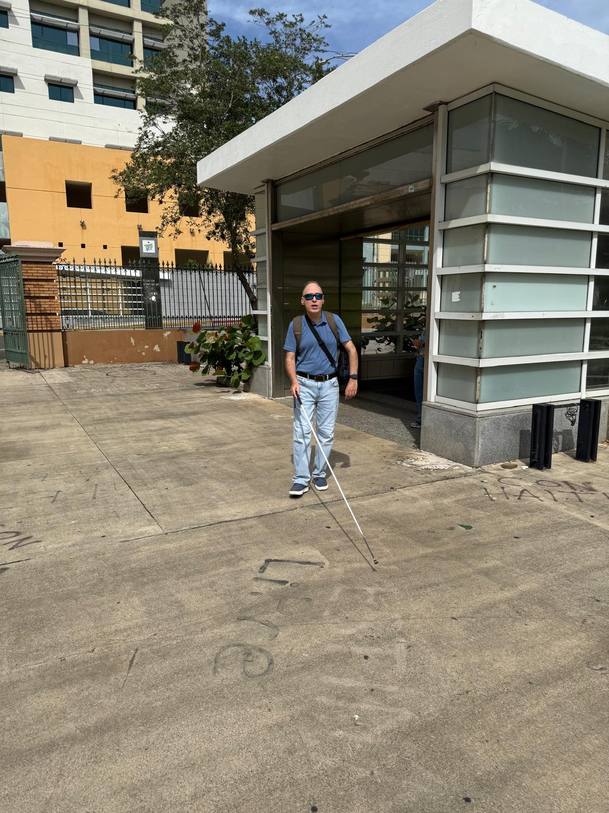 La foto presenta a Manolo caminando por la universidad utilizando su bastón y las gafas Meta.